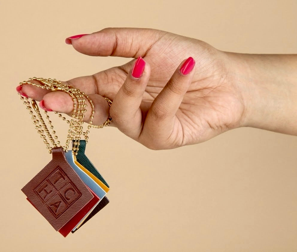 Hand holding five small chocolate bar-shaped pendants on a beige background.