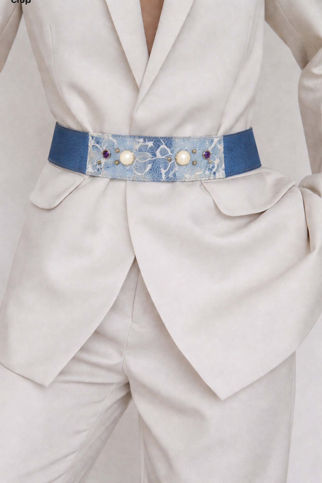 Close-up of a white suit with a decorative blue belt featuring pearls and stones.