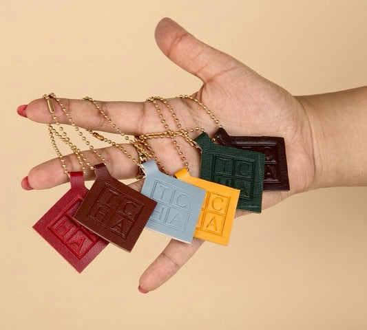 Hand holding five small chocolate bar-shaped pendants on a beige background.