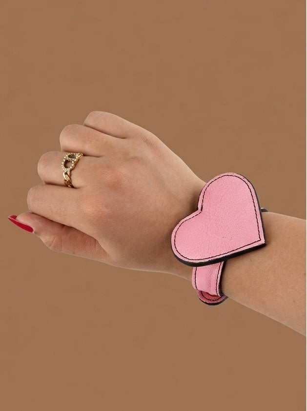Hand wearing a pink heart-shaped wristband on a brown background