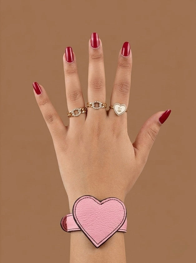 Hand wearing pink heart shaped leather bracelet on a brown background
