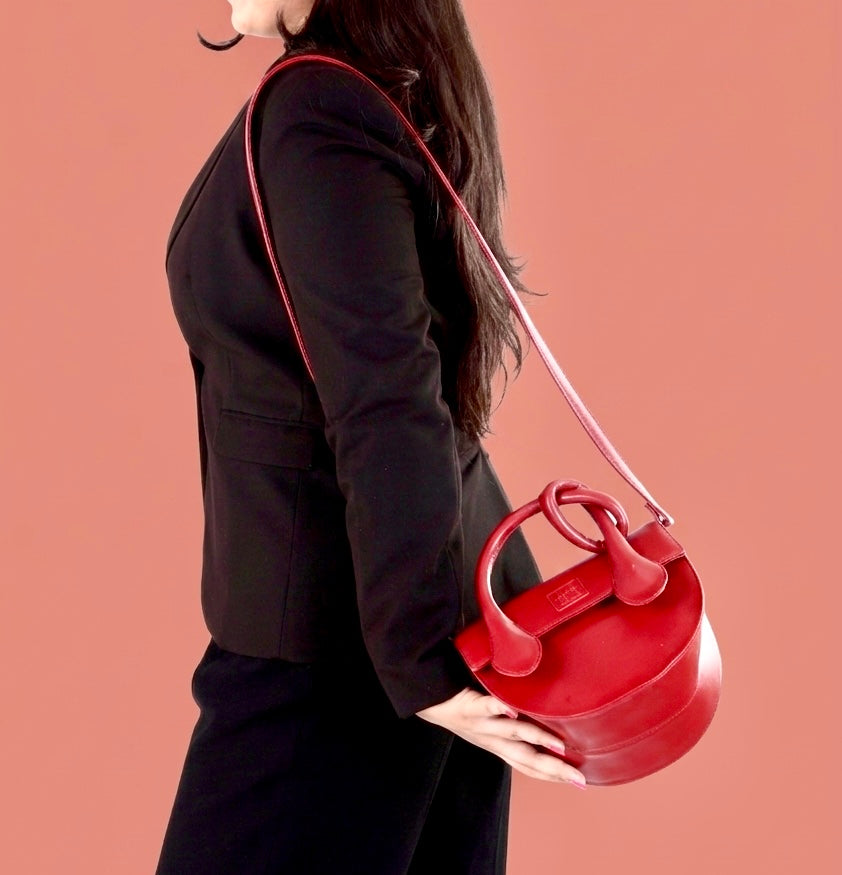 Person holding a red handbag against a pink background